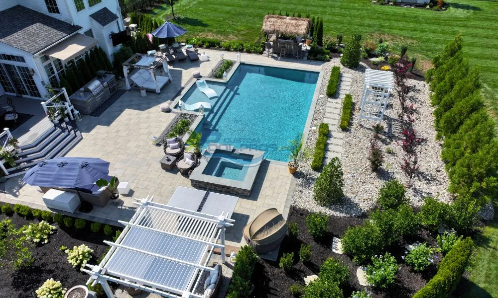 Aerial view of a luxurious backyard featuring a rectangular swimming pool, a hot tub, and stylish lounge furniture surrounded by landscaped greenery and stone pathways, luxury swimming pools