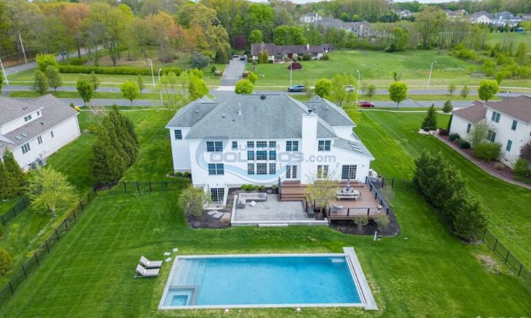 Aerial view of a modern two-story white house with a spacious backyard, featuring a swimming pool and a wooden deck surrounded by lush green landscaping, nj pool builders