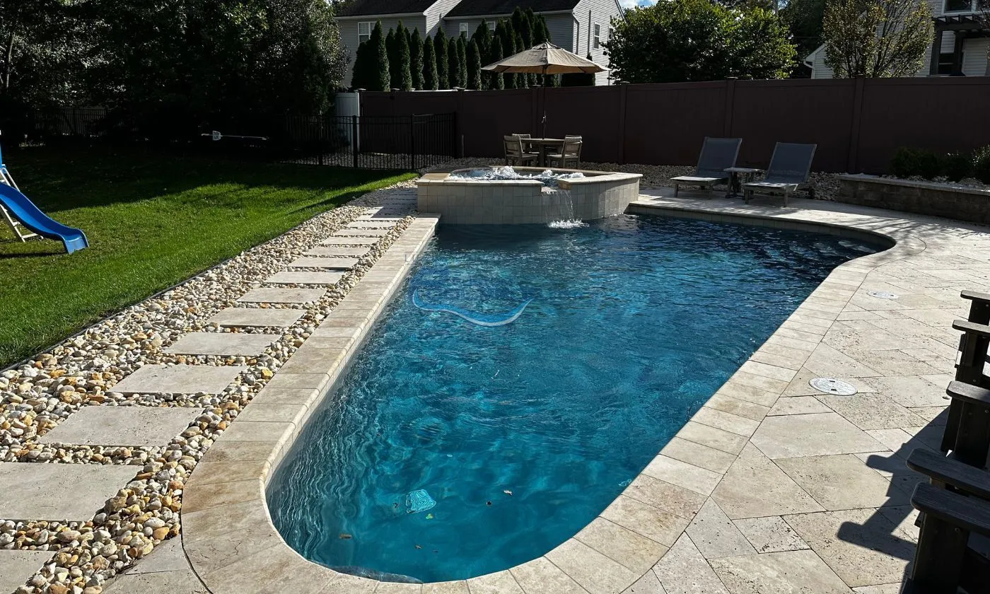 custom inground triangular shaped freeform inground pool installation with spa surrounded by travertine pool deck, luxury pools